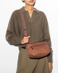 model wearing a brown sweater and green trousers wearing the mz wallace Crosby Ella Crossbody Terracotta on a grey background