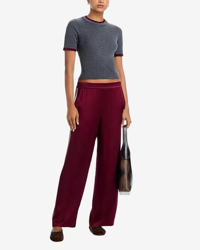 Woman wearing a gray cropped top and burgundy pants holding a black handbag on a white background