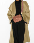 model wearing a black sweater, black trousers, and green trench coat and the wallace Small Metro Tote Camera Bag Terracotta on a grey background