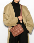 model wearing a black sweater, black trousers, and green trench coat and the wallace Small Metro Tote Camera Bag Terracotta on a grey background