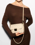 MZ Wallace Small Crosby Lock Crossbody Buff Crossbody worn by model wearing brown off the shoulder dress in front of white background. 