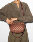 model wearing a brown sweater and green trousers holding  the mz wallace Crosby Ella Crossbody Terracotta on a grey background