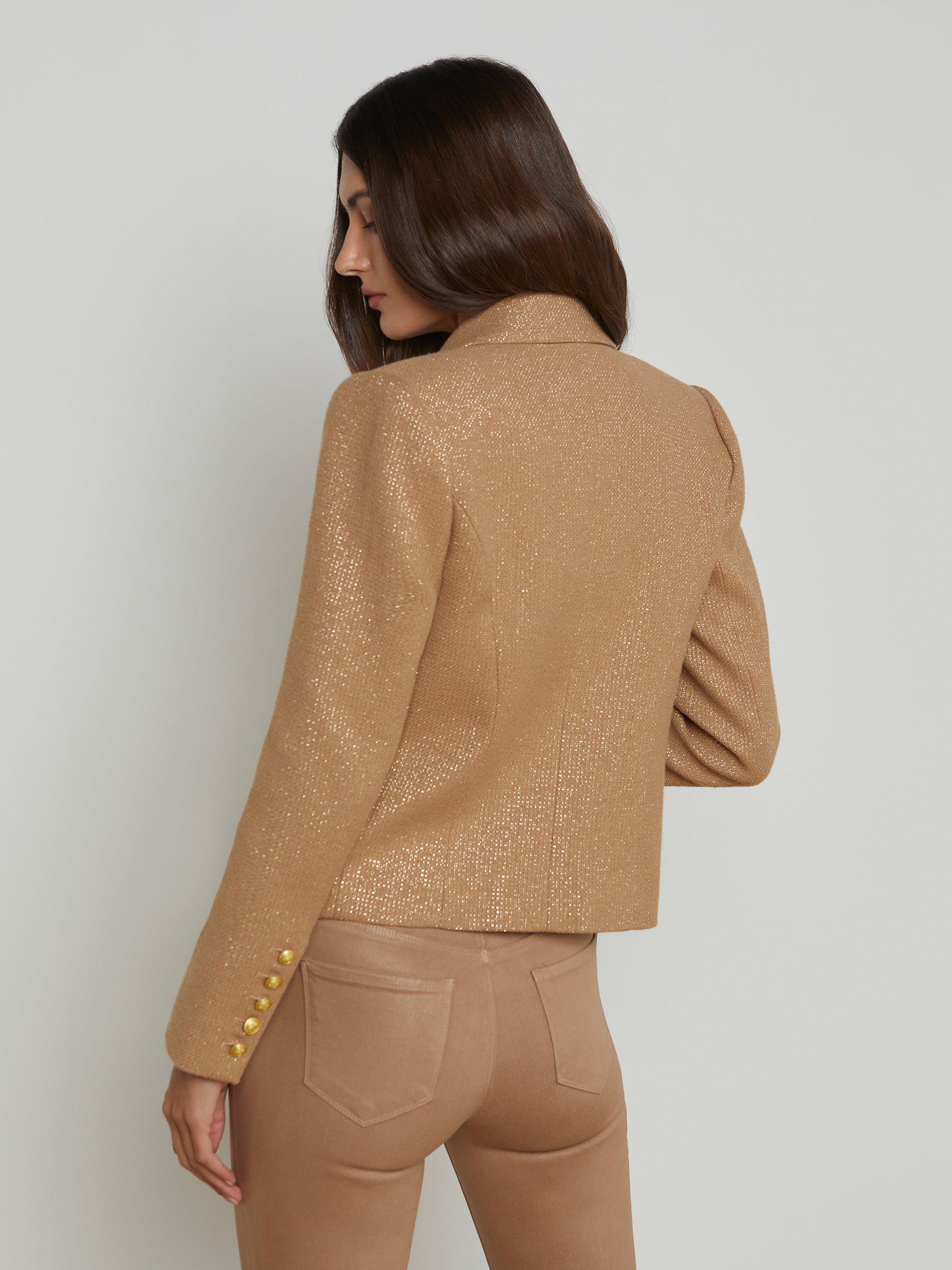 upper half back view of a brunette model wearing the l'agency Brooke double breasted crop blazer in latte/gold with tan pants and a brown belt