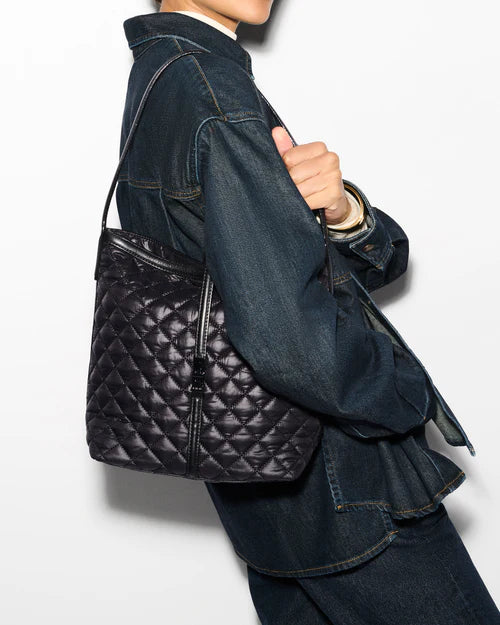 right facing model wearing a white turtleneck, denim jacket, jeans, and a black belt and wearing the mz wallace Small Astor Hobo Black on a grey background