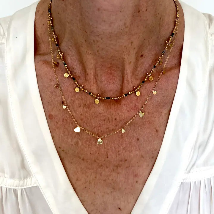 close up of a lady's neck wearing the Ma Cocotte Lola Necklace  and a beaded necklace. she's wearing a white v-neck blouse