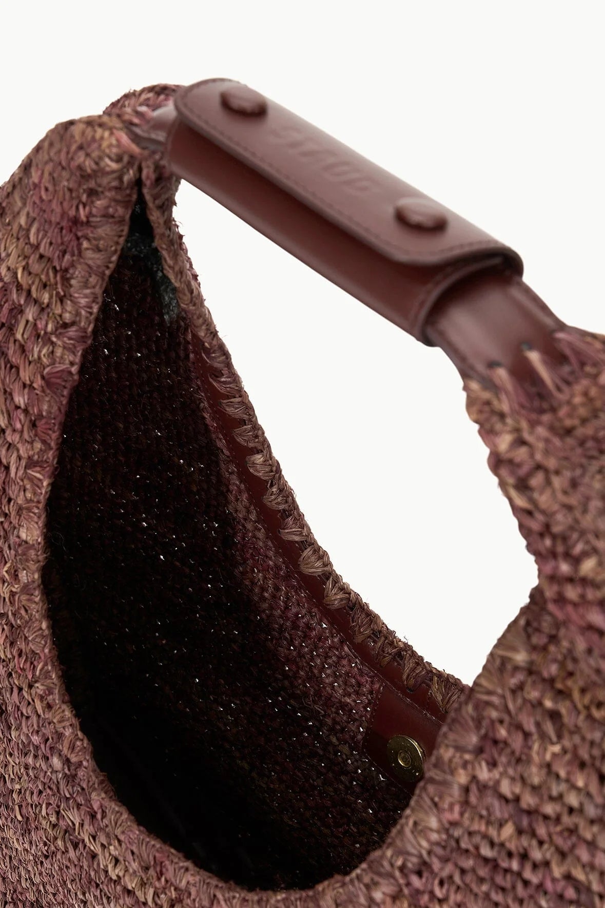 close up view of the handle of the Staud Large Raffia Moon Tote Bag in Mahogany with white background