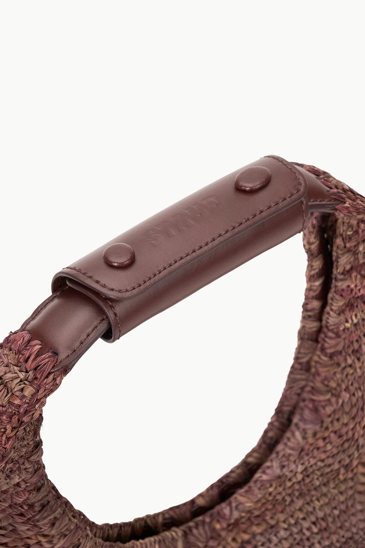 close up view of the handle of staud moon raffia tote bag in mahogany with white background