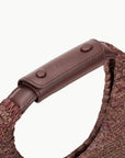 close up view of the handle of staud moon raffia tote bag in mahogany with white background