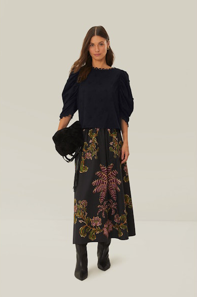 Front view of Brunette woman wearing farm rio 3D Flowers Blouse in Black with a floral skirt, black purse, and black boots with a white background