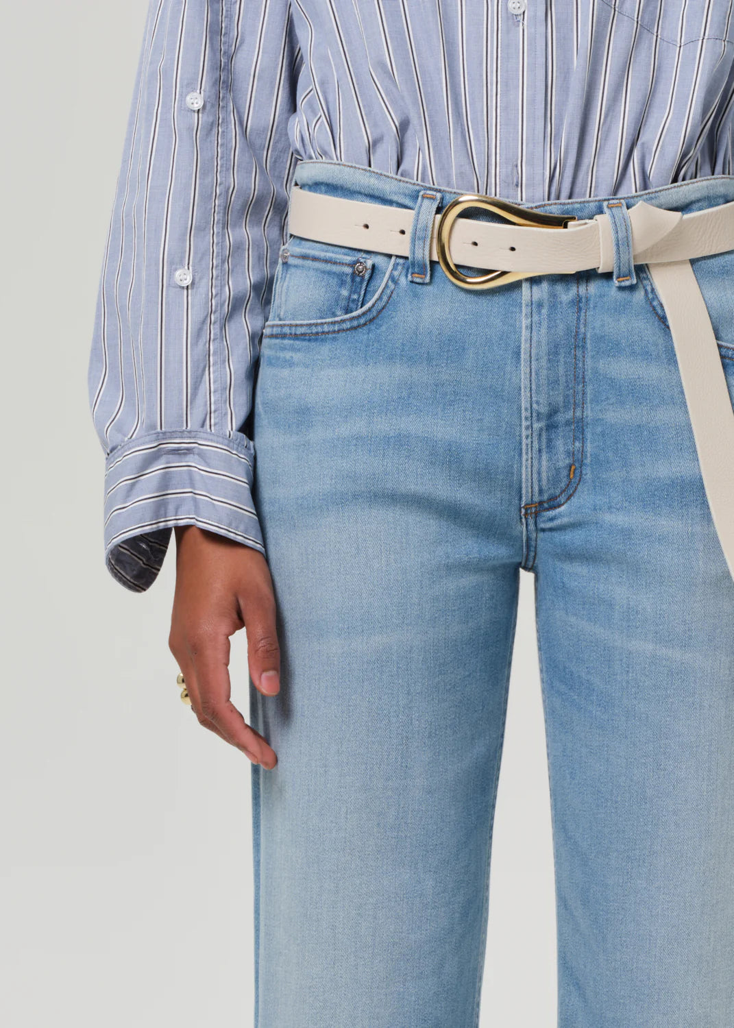 close up of model wearing the citizens of humanity Palma Straight Lisbon with a white belt, tan sandals, and a blue striped button down on a white background from her torso to knee