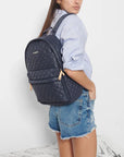 model wearing mz Wallace city metro backpack dawn on white background, denim shorts and a blue button down