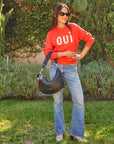 brunette model outside in the grass wearing a Oui sweatshirt and jeans and snakeskin boots holding the Clare v Moyen Messenger Black Woven Zig Zag 