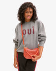 black model wearing a grey Oui sweatshirt and black track pants and wearing the Clare v Petit Moyen Messenger Bright Poppy/Bordeaux Woven Checker on a white background