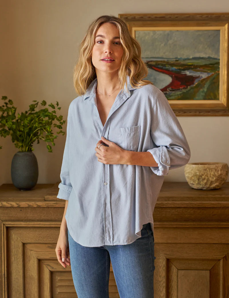 front view of blonde model wearing the frank & eileen Eileen Relaxed Button Up Gray Blue with jeans in front of a console table and art