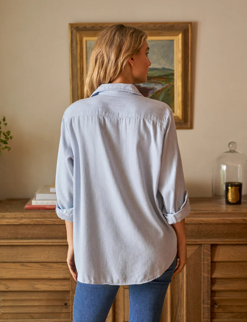 back view of blonde model wearing the frank & eileen Eileen Relaxed Button Up Gray Blue with jeans in front of a console table and art