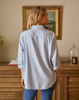 back view of blonde model wearing the frank & eileen Eileen Relaxed Button Up Gray Blue with jeans in front of a console table and art