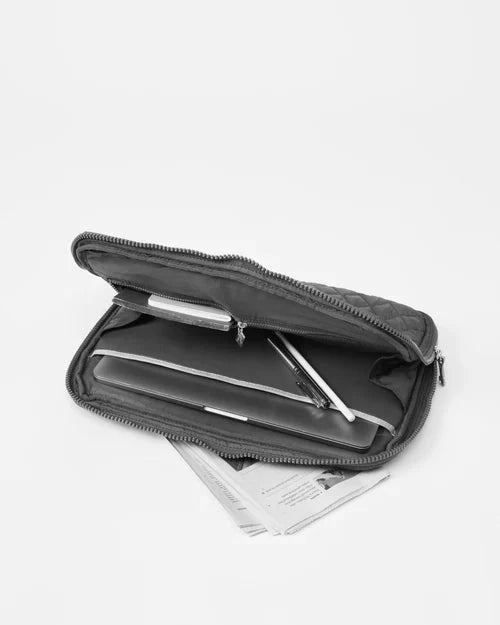 Interior view of MZ Wallace Metro Organizer Black Cosmetic with a laptop in the interior pocket and note pads in the mesh zipper pocket and pens in the open part of bag, in front of a white background. 