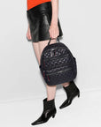 lower half of model wearing a black leather skirt and orange tee holding the mz Wallace Small Crosby Backpack Black on a white background