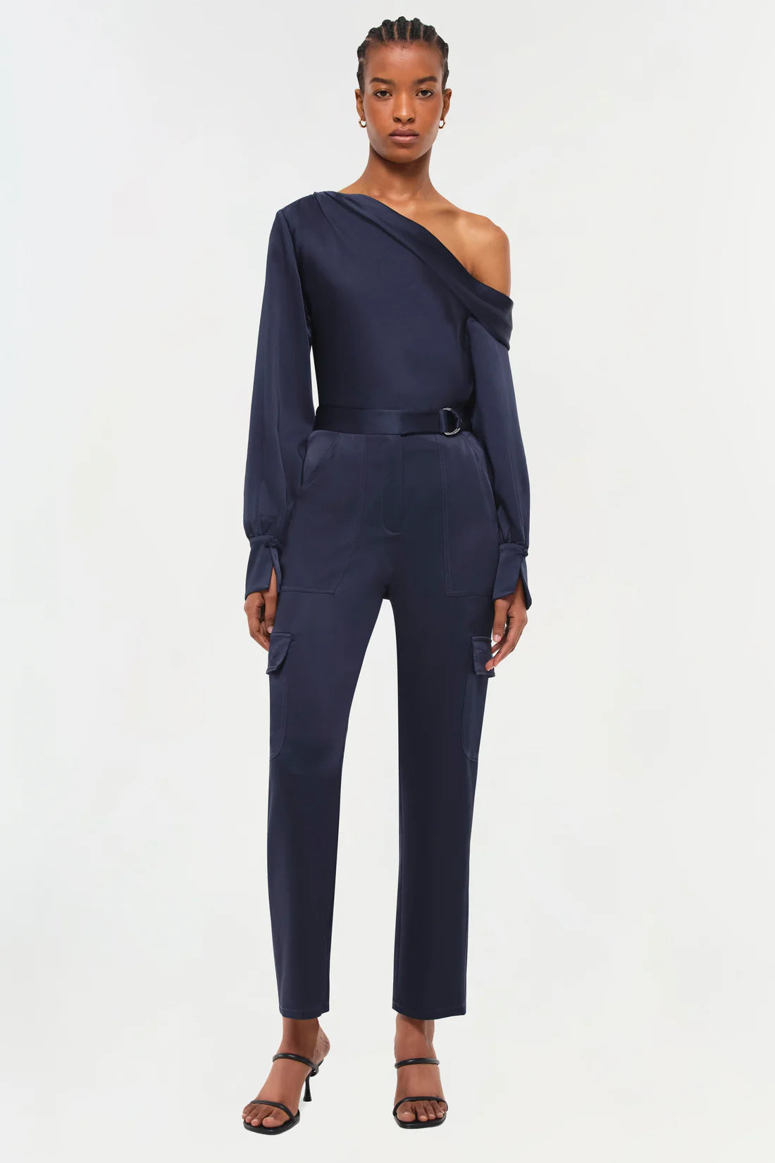 full front view of model on a white background wearing the simkhai Carolina utility pant in midnight with a matching blue blouse and black strappy heels