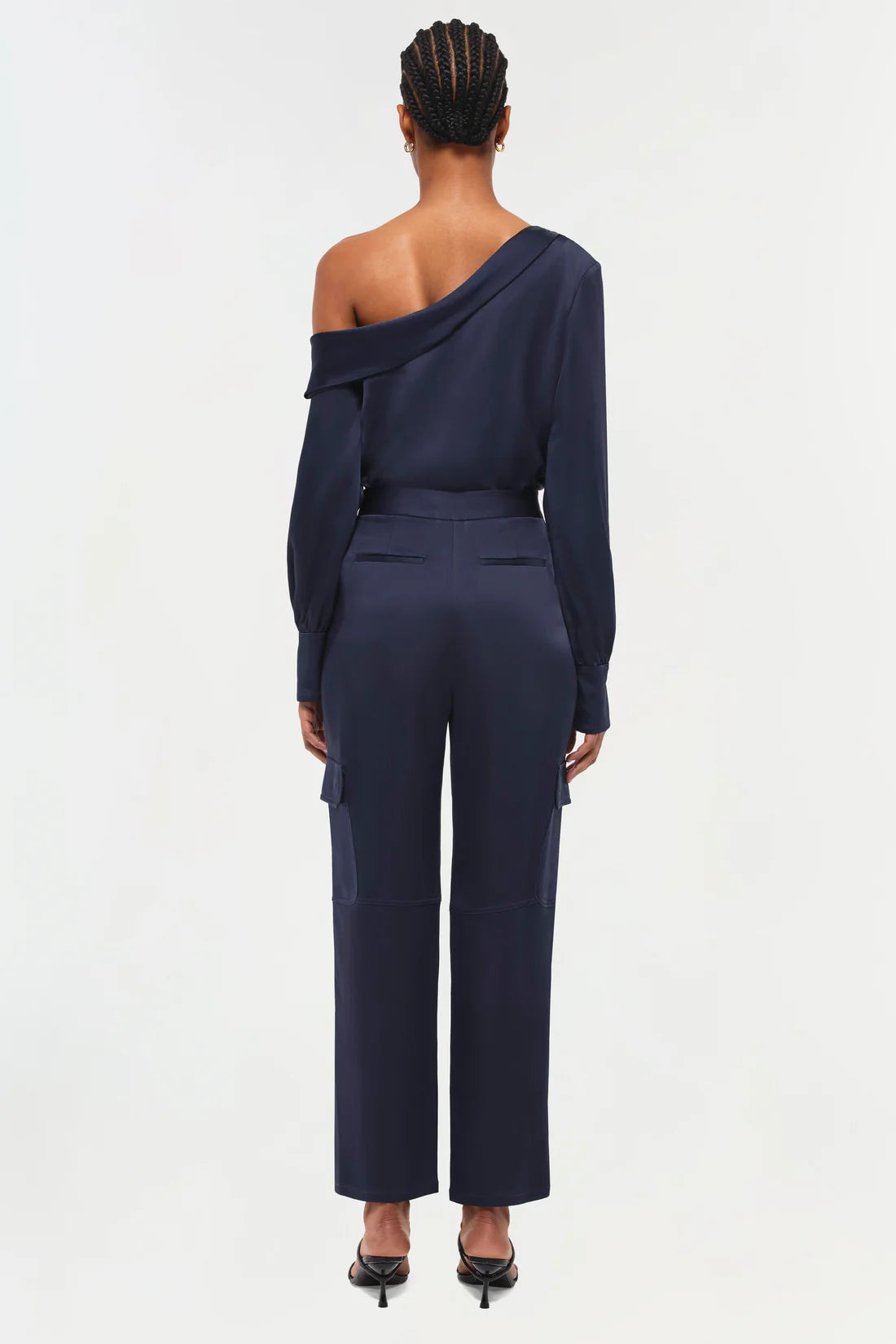 full back view of model on a white background wearing the simkhai Carolina utility pant in midnight with matching blouse and black strappy heels