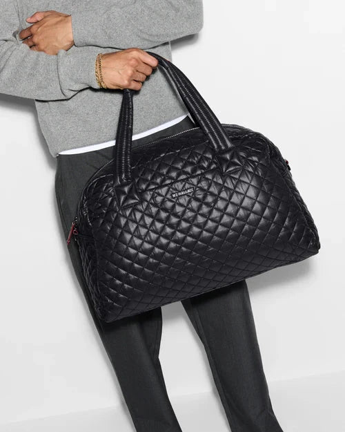 MZ Wallace Travel Jim Black Tote & Satchel held by a model using straps wearing grey sweatshirt and dark pants.
