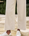 Close up view of knee down on the frank & eileen Wexford Trouser Cement on a black model with white sneakers and a white blouse on a patio in front of greenery